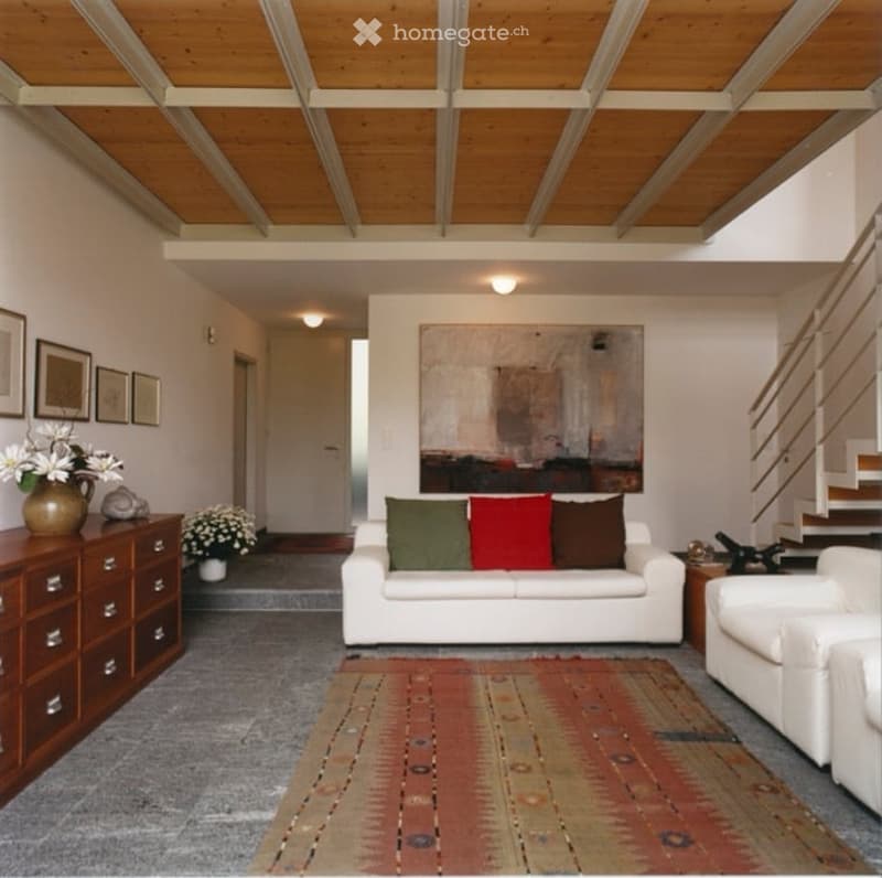 Living room with a white sofa, armchair, wooden dresser, vase with flowers, and artwork on the wall.