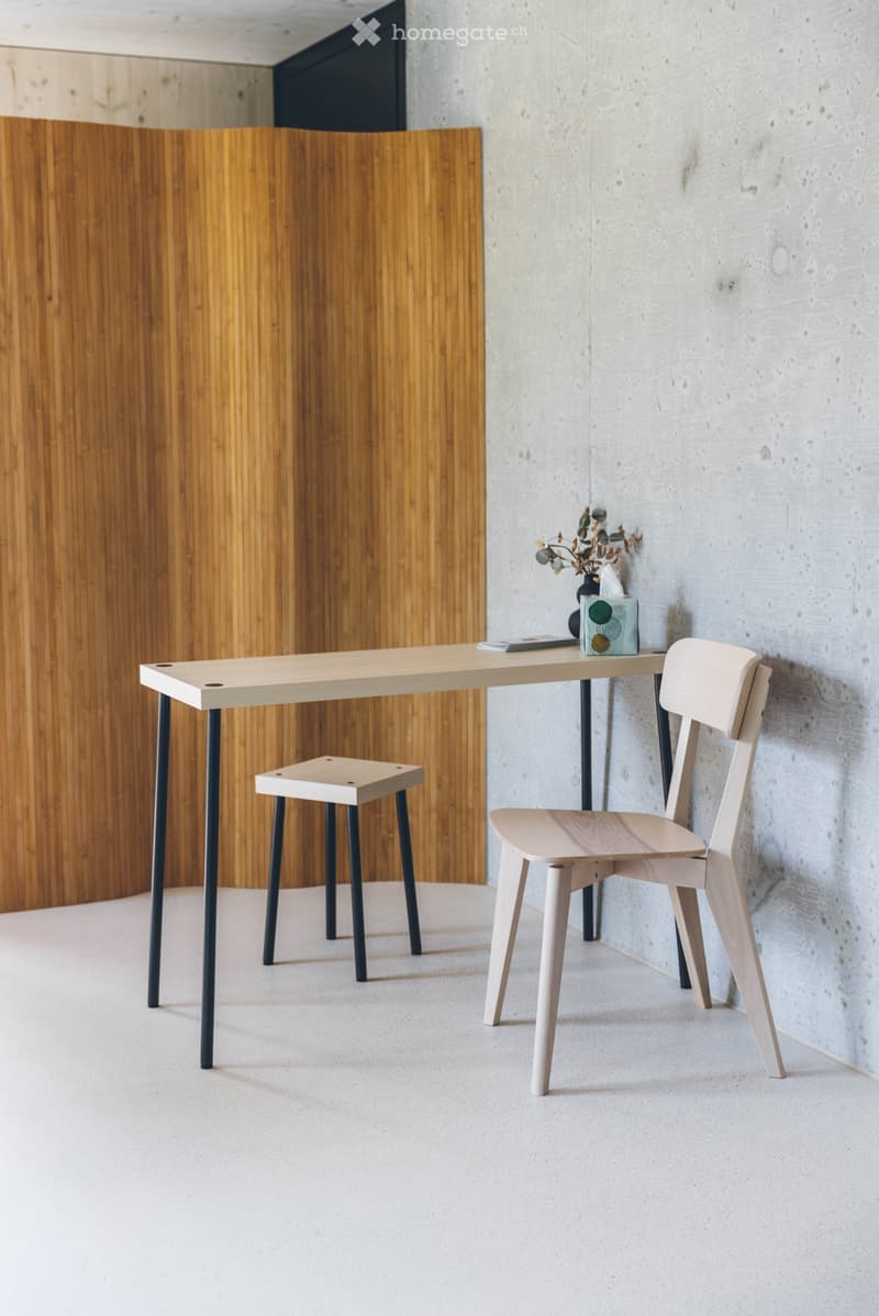 Minimalist room with a light wooden table, two chairs, a small stool, and a vase with dried flowers on the table.