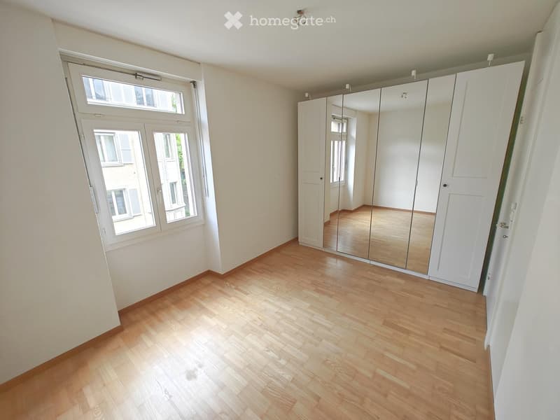 Empty room with wooden flooring, large windows, and a mirrored wardrobe unit.