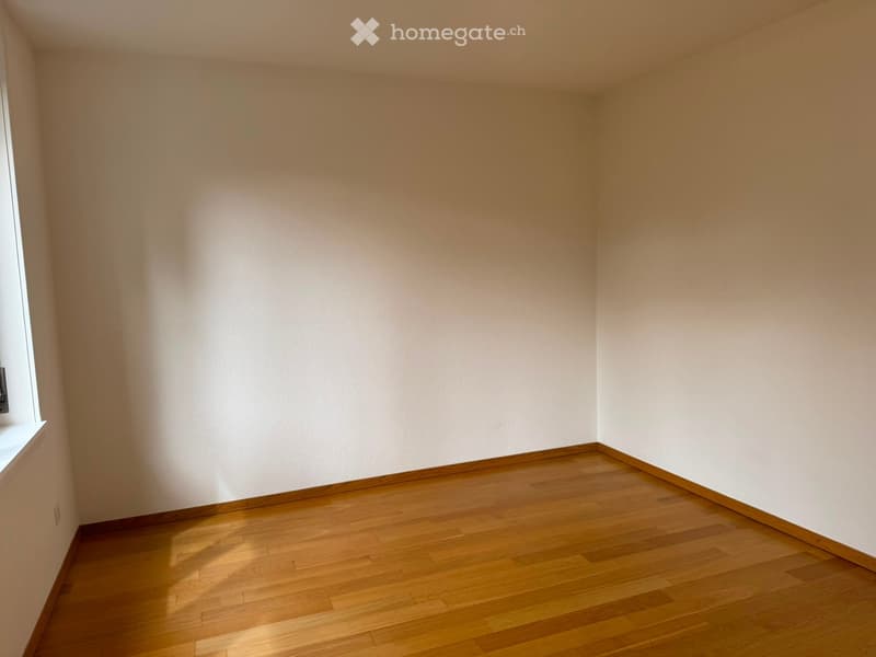Empty room with wooden flooring and white walls, featuring a small window on one side.