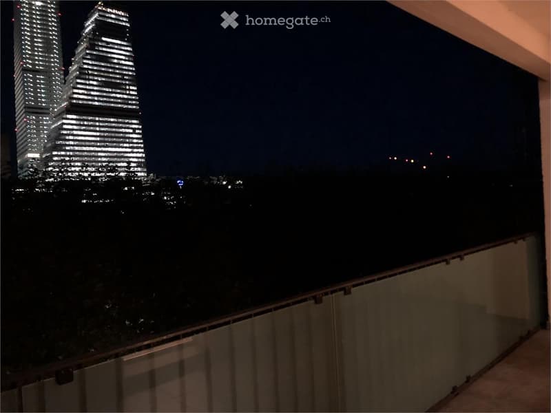 Nighttime view from a balcony showing illuminated skyscrapers in the distance.