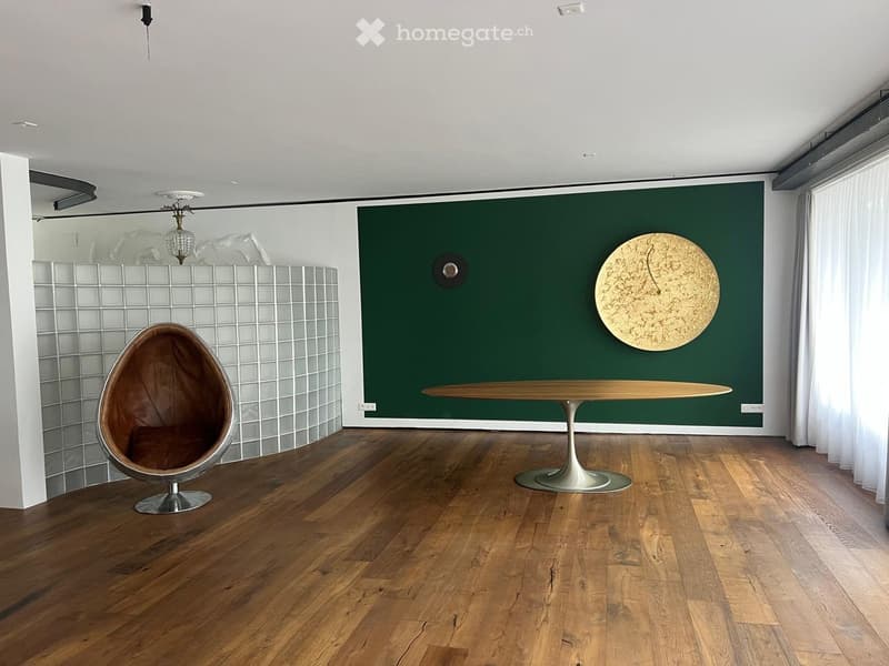 Modern room with wooden floor, green accent wall, a round wooden table, a unique egg-shaped chair, and a large wall clock.
