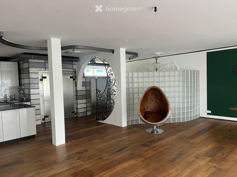Open-plan living and kitchen area with wooden flooring, white kitchen cabinets, a modern sink, and a distinctive egg-shaped chair.