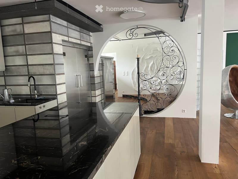 Modern kitchen with black marble countertops, stainless steel sink, and a decorative candle holder near an arched doorway.