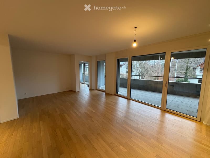 Empty room with wooden flooring, large sliding glass doors leading to a balcony, and neutral-colored walls.