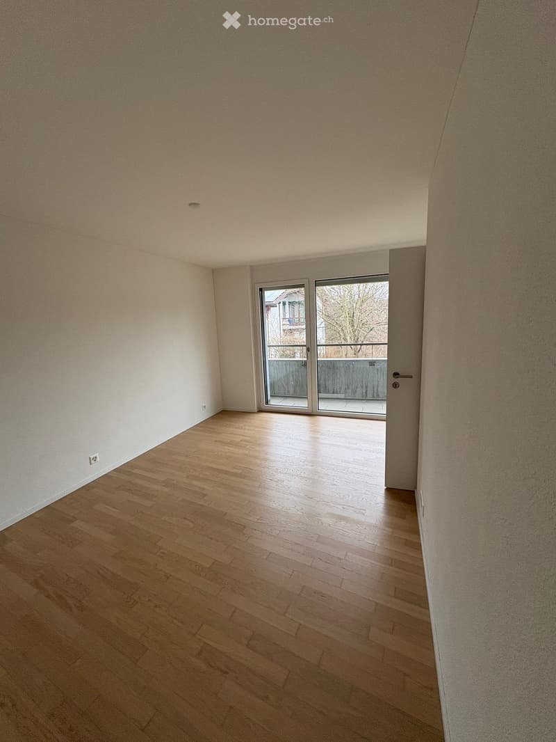 Empty room with wooden flooring, white walls, and a sliding glass door leading to a balcony.