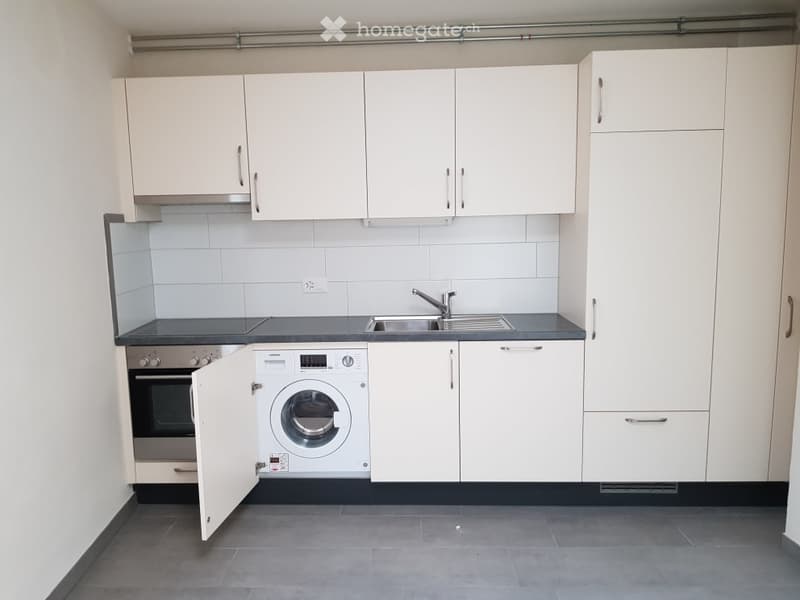 Modern kitchen with white cabinets, stainless steel sink, oven, and washing machine.