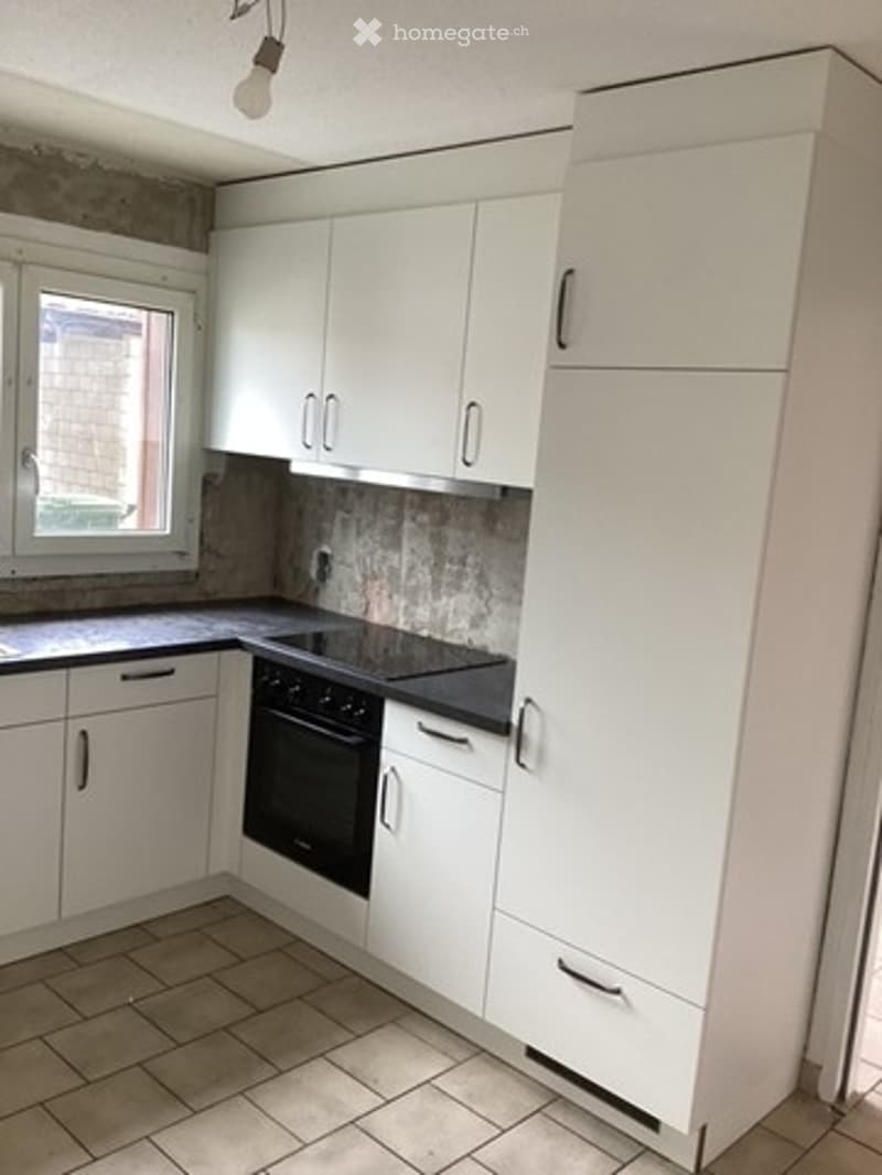Modern kitchen with white cabinets, black countertop, and built-in oven. Features a tiled floor and a window with a view of a brick wall.