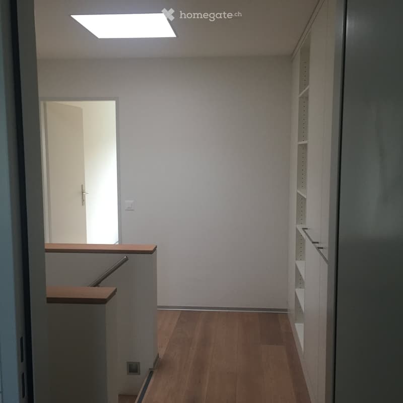 Empty hallway with wooden flooring, white walls, and a staircase leading upwards. A door is visible at the end of the hallway.
