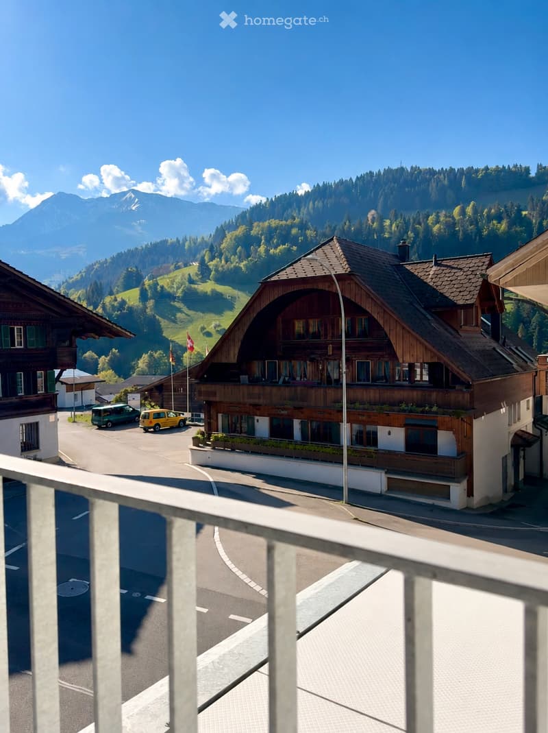 A large wooden building with a balcony overlooking a picturesque village and mountain landscape.