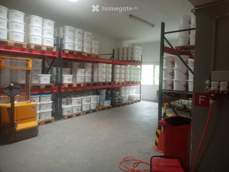 Warehouse with concrete floor, metal shelving units, and numerous white buckets stacked on pallets. A yellow forklift is visible on the left side.