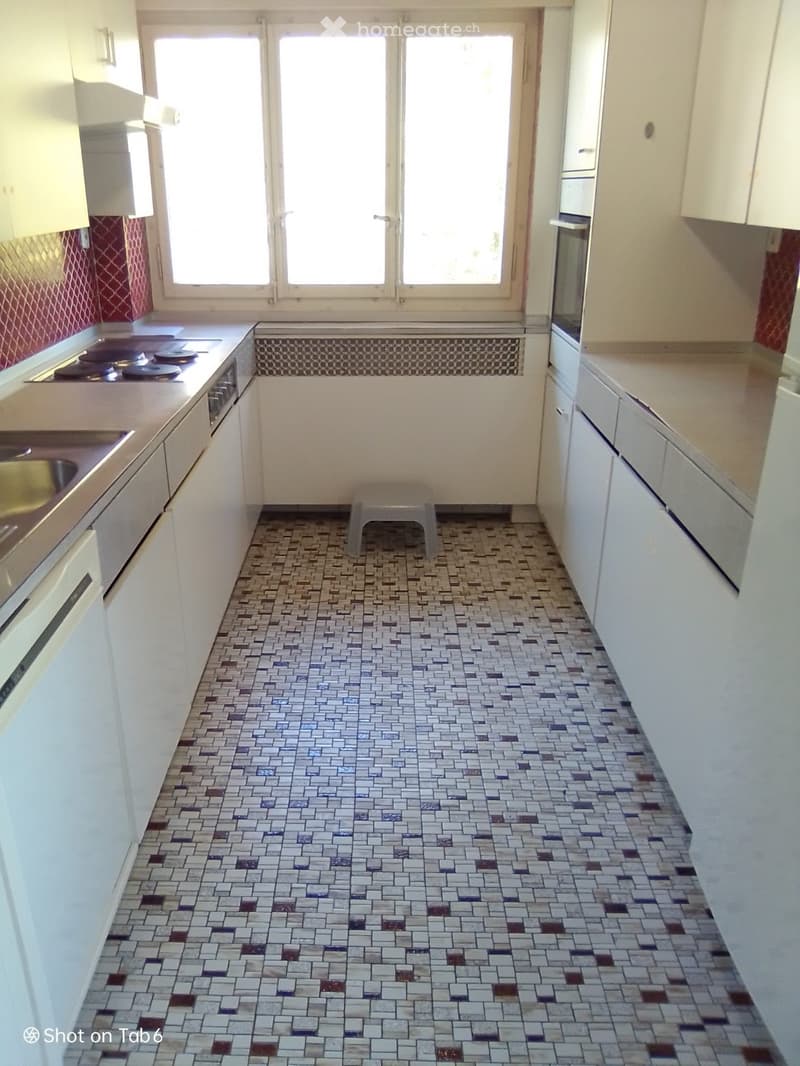 Kitchen with white cabinets, tiled floor, stove, sink, and a small stool in the center.