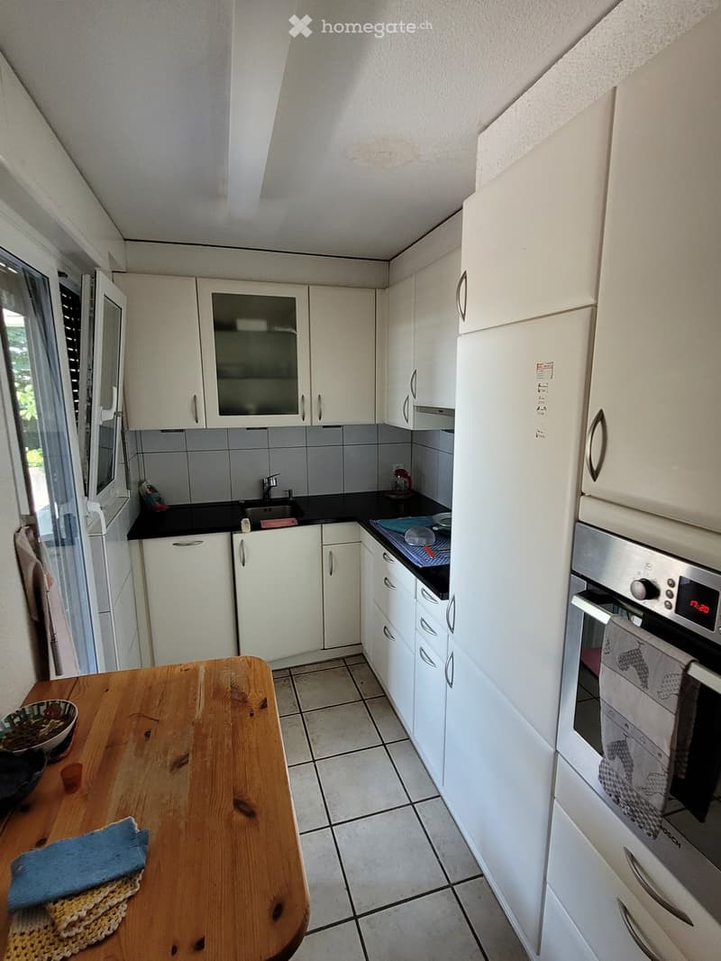 Modern kitchen with white cabinets, stainless steel appliances, and a wooden table with a bowl and cloth.