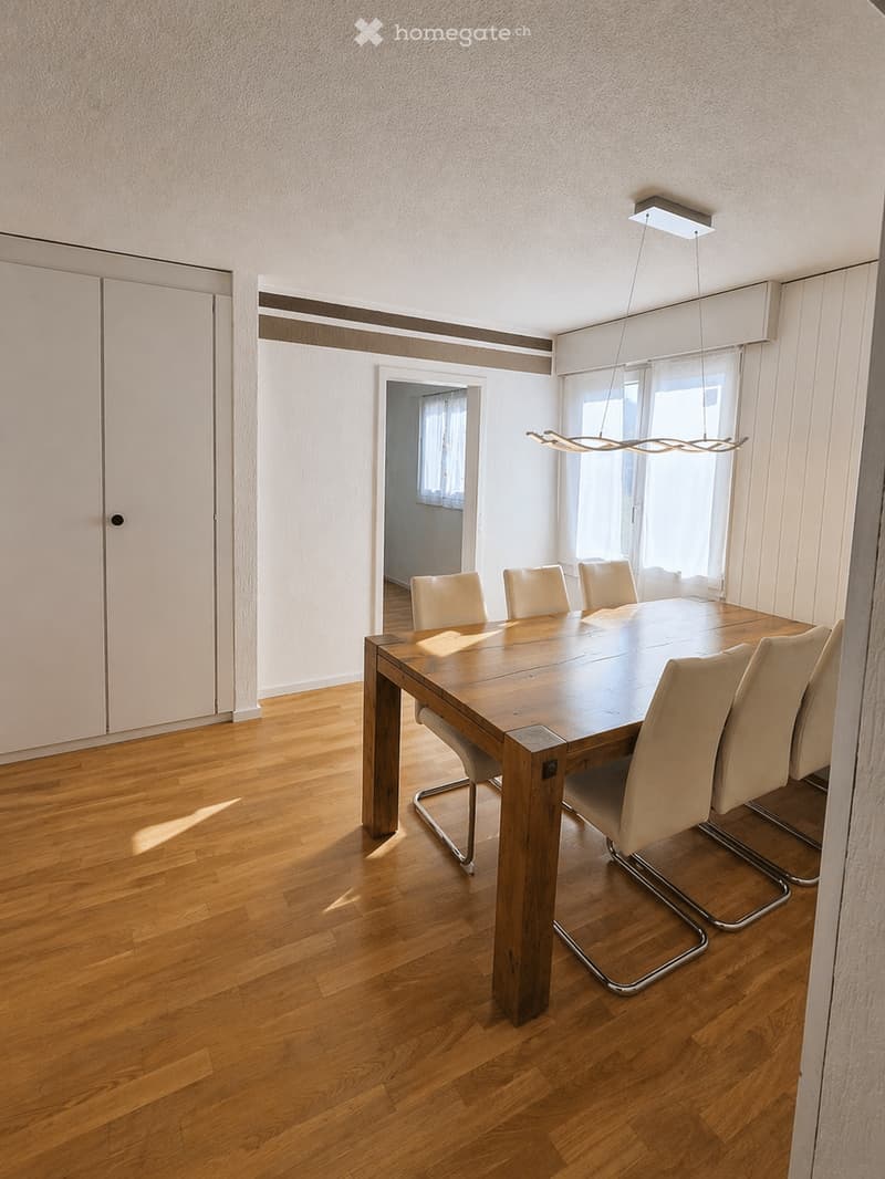 Dining room with a wooden dining table and four chairs, large windows, modern lighting fixture, and wooden flooring.