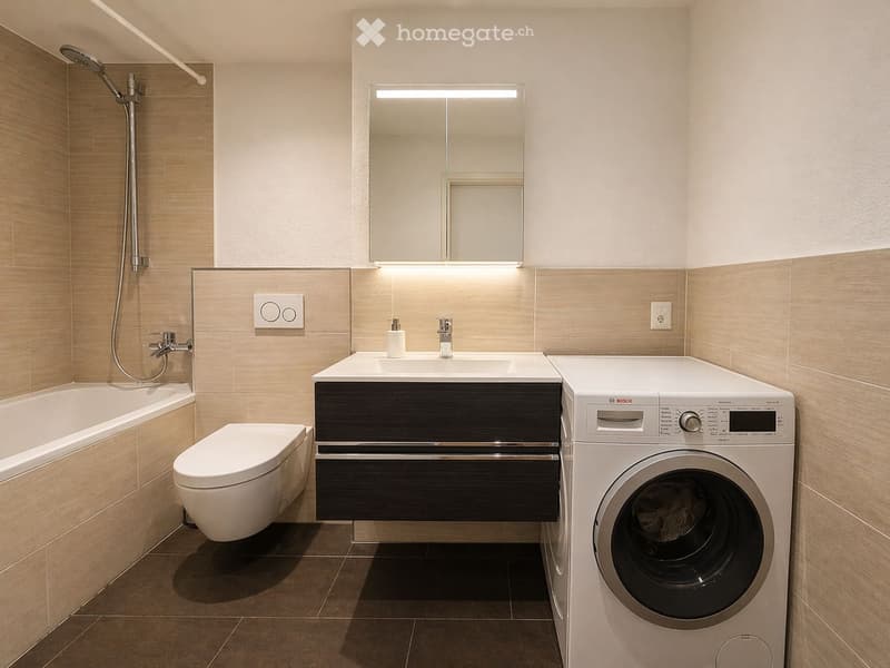 Modern bathroom with a bathtub, toilet, sink, mirror, and a Bosch washing machine. Features include a sleek vanity with a built-in sink and a showerhead with a handheld sprayer.
