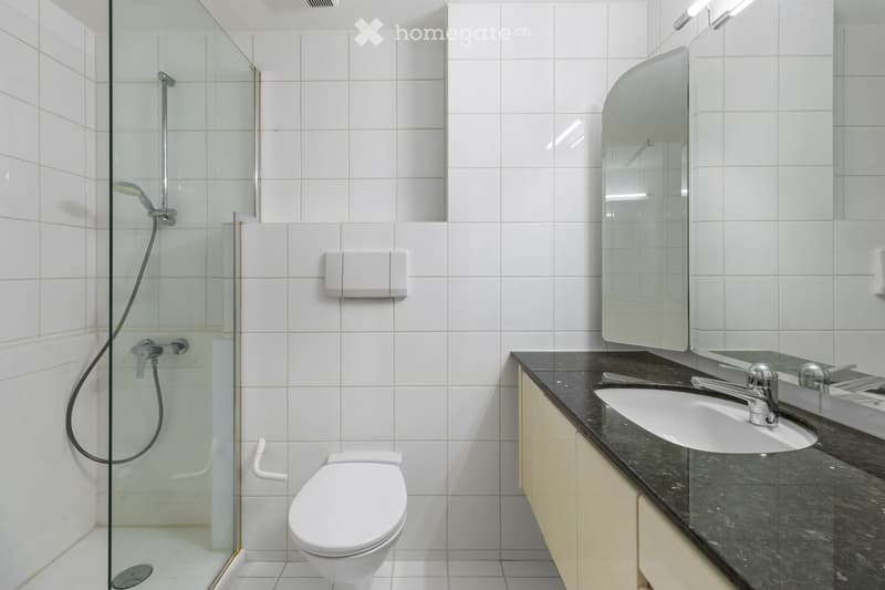 Bathroom. Modern bathroom with white tiles, glass shower enclosure, white toilet, sink, and mirror.