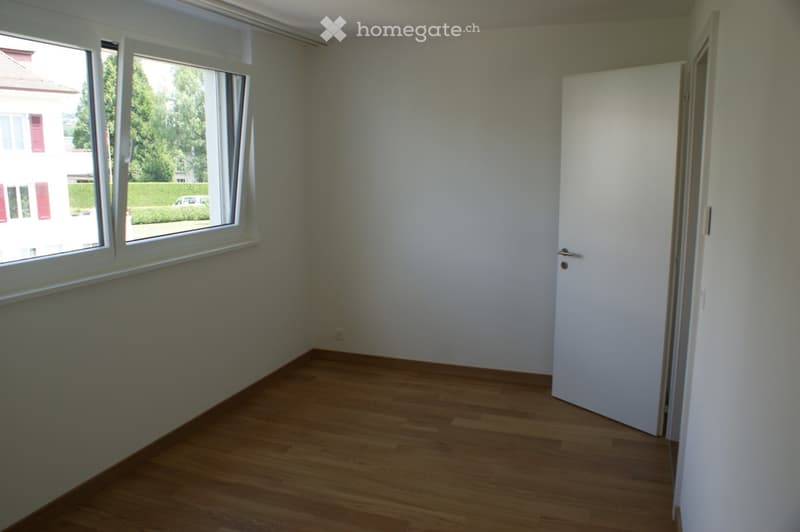 Empty room with wooden flooring, white walls, large window, and a closed door.