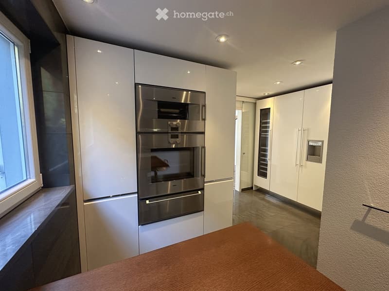 Modern kitchen with white cabinets, stainless steel oven, refrigerator, and a wooden table.