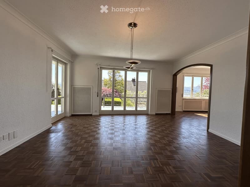 Empty room with wooden parquet flooring, large windows, and a ceiling light fixture. No furniture or equipment present.