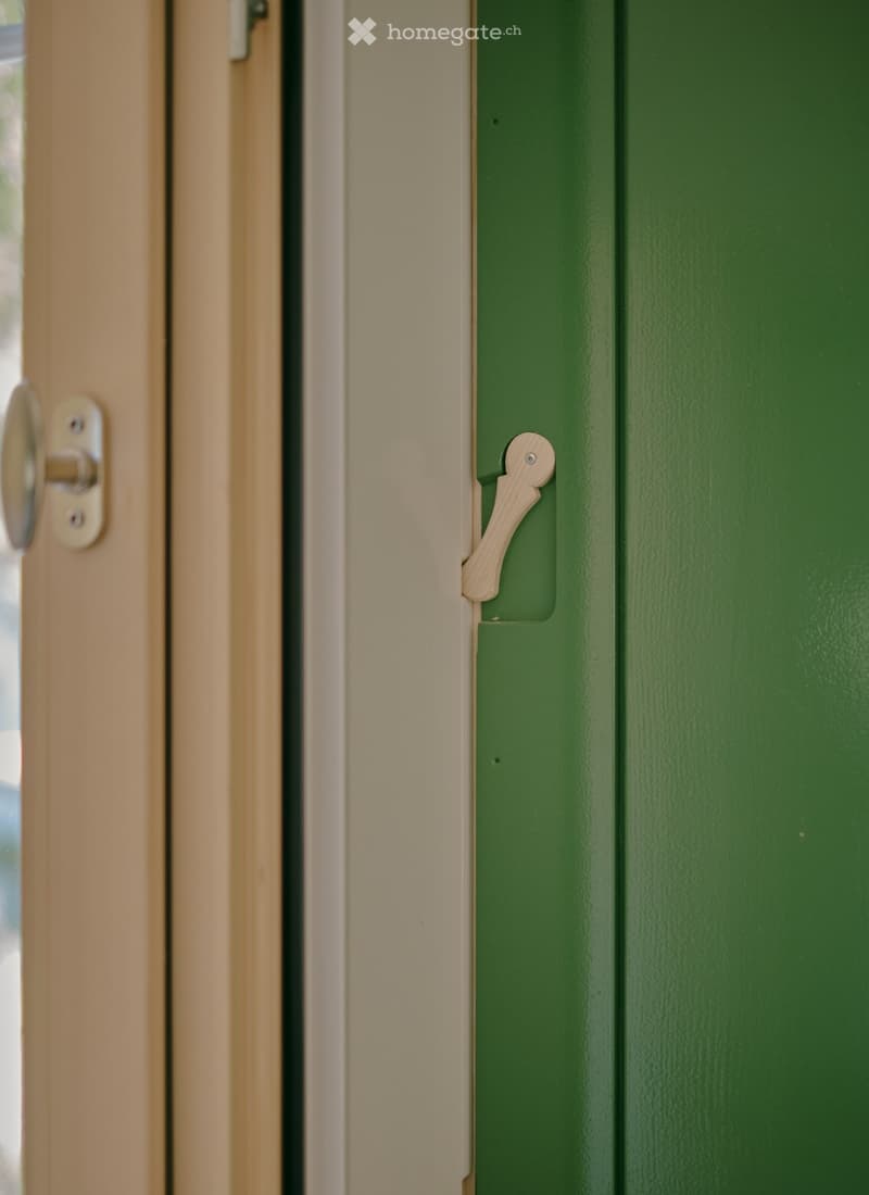Close-up view of a green door with a wooden handle and a silver latch mechanism, set within a light-colored frame.