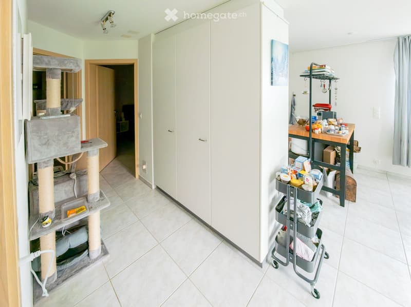 A small, well-lit room with a cat tree on the left, a kitchen cart on the right, and a doorway leading to another room.