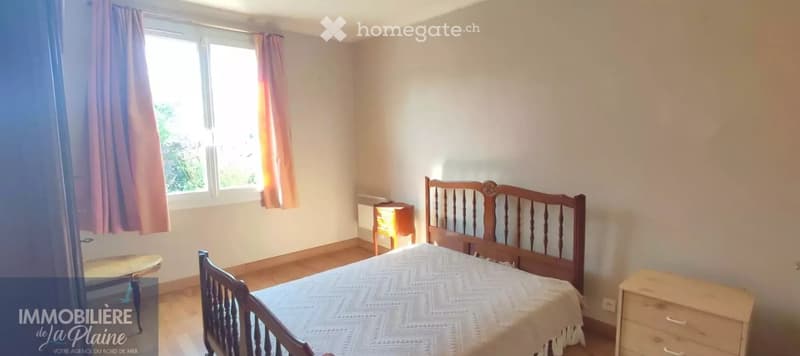 Bedroom with wooden bed, nightstands, a small chair, and a radiator near the window.