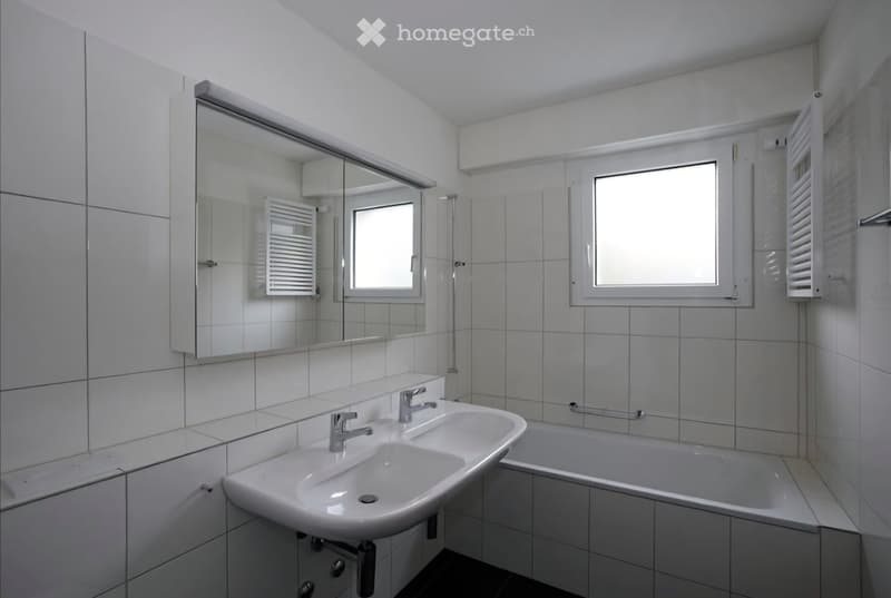 Modern bathroom with white tiles, a double sink, a bathtub, a large mirror, and a radiator.