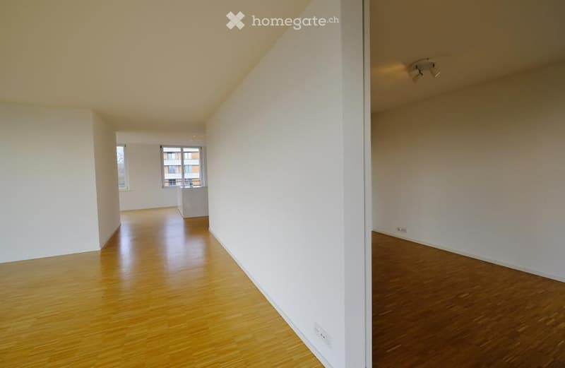 Empty unfurnished room with wooden flooring, white walls, and large windows. No furniture or equipment present.