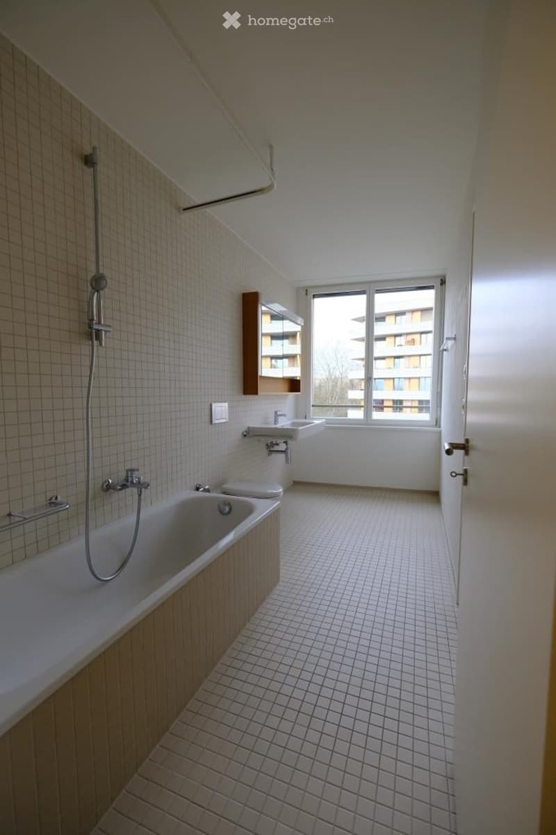 Modern bathroom with white tiled walls and floor, featuring a bathtub, shower, sink, toilet, and a built-in cabinet with a mirror.