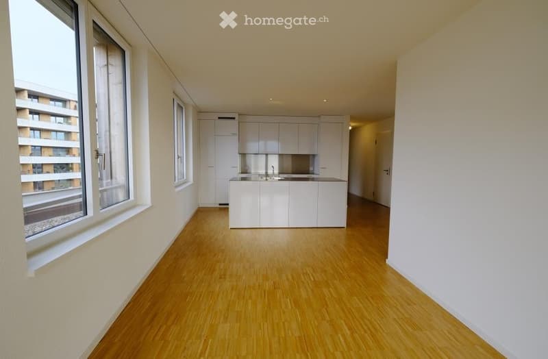 Open-plan kitchen and living area with light wood flooring, white cabinetry, and large windows offering a city view.