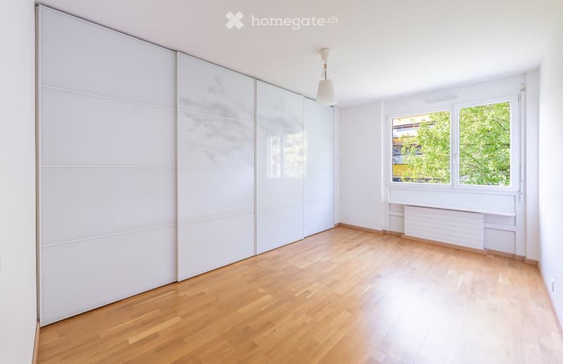 Unfurnished Room. Empty room with wooden flooring, white walls, large sliding closet doors, and a window with a view of greenery.