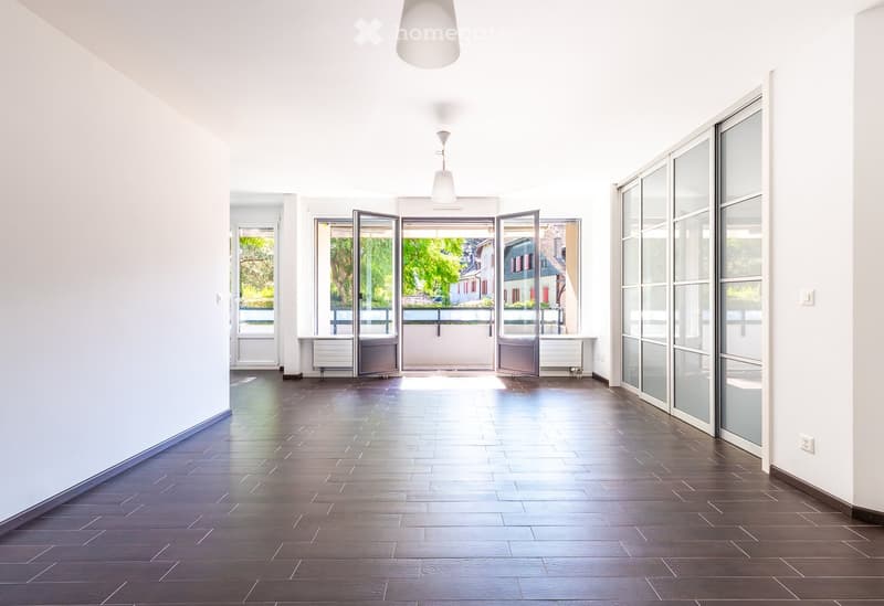Corridor / Hallway. Bright, modern hallway with dark wooden flooring, white walls, and large glass doors leading to an outdoor area. Minimalist design with pendant lights and a sleek, open layout.