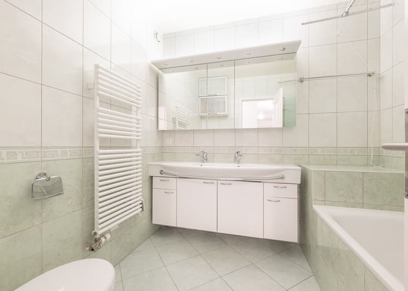 Bathroom. Modern bathroom with white tiles, a double sink vanity, a large mirror, a bathtub, and a white radiator.