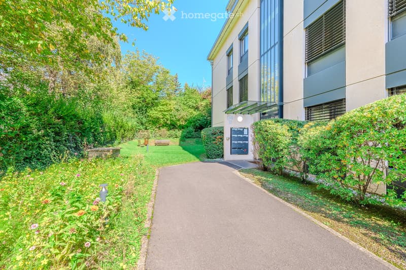 Garden / Outdoor Area. A well-maintained garden path leads to a modern building entrance, surrounded by lush greenery and flowering plants.
