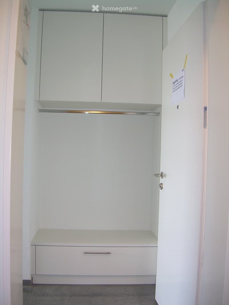Empty closet with white cabinets, shelves, and drawers, featuring a tiled floor and a partially open door.