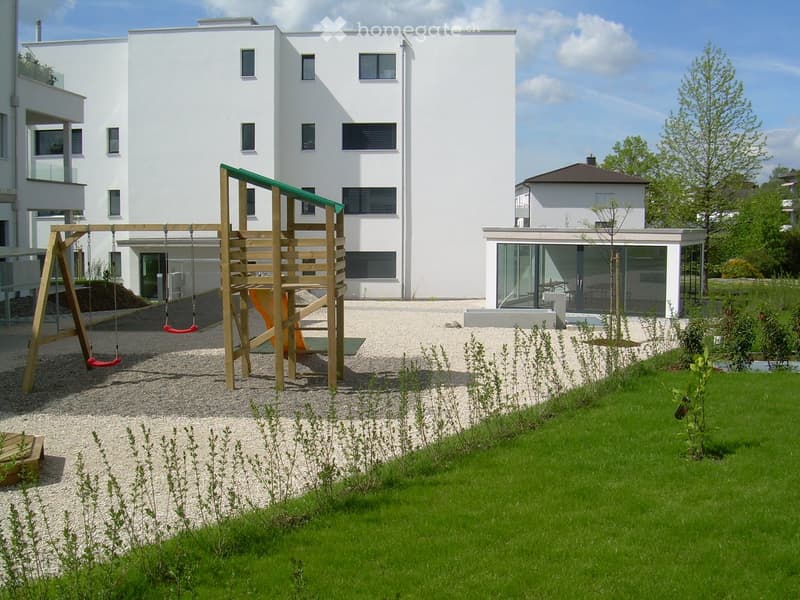 Modern residential complex with a playground, grassy lawn, and contemporary buildings.