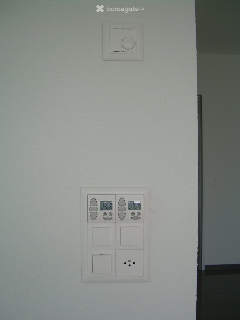 A hallway with modern light switches and a digital display showing the time and temperature.