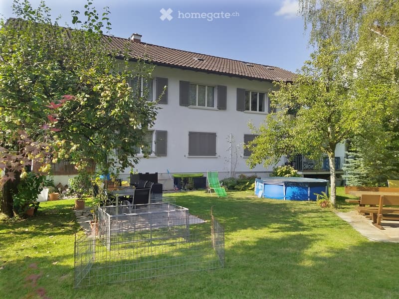 Well-maintained garden with a fenced area, outdoor furniture, a small pool, and a house with multiple windows and shutters.