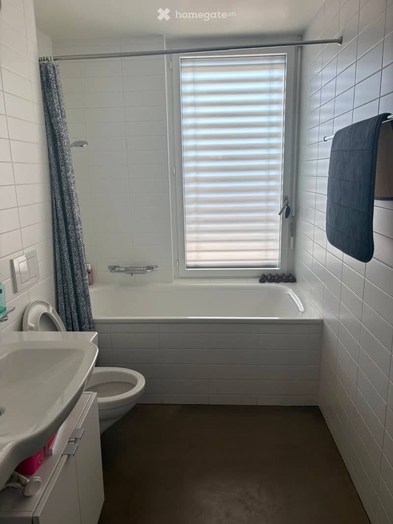 Modern bathroom with white tiles, a bathtub, a sink, a toilet, a towel, and a shower curtain.