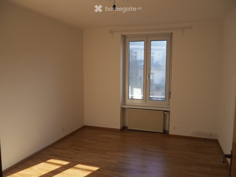 Unfurnished Room. Empty room with wooden flooring, white walls, and a large window with a radiator underneath.
