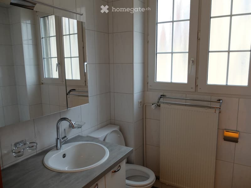 Bathroom. Modern bathroom with a white sink, chrome faucet, toilet, mirror cabinet, radiator, and towel rack. The walls are tiled in light beige, and the floor is covered with marble tiles.