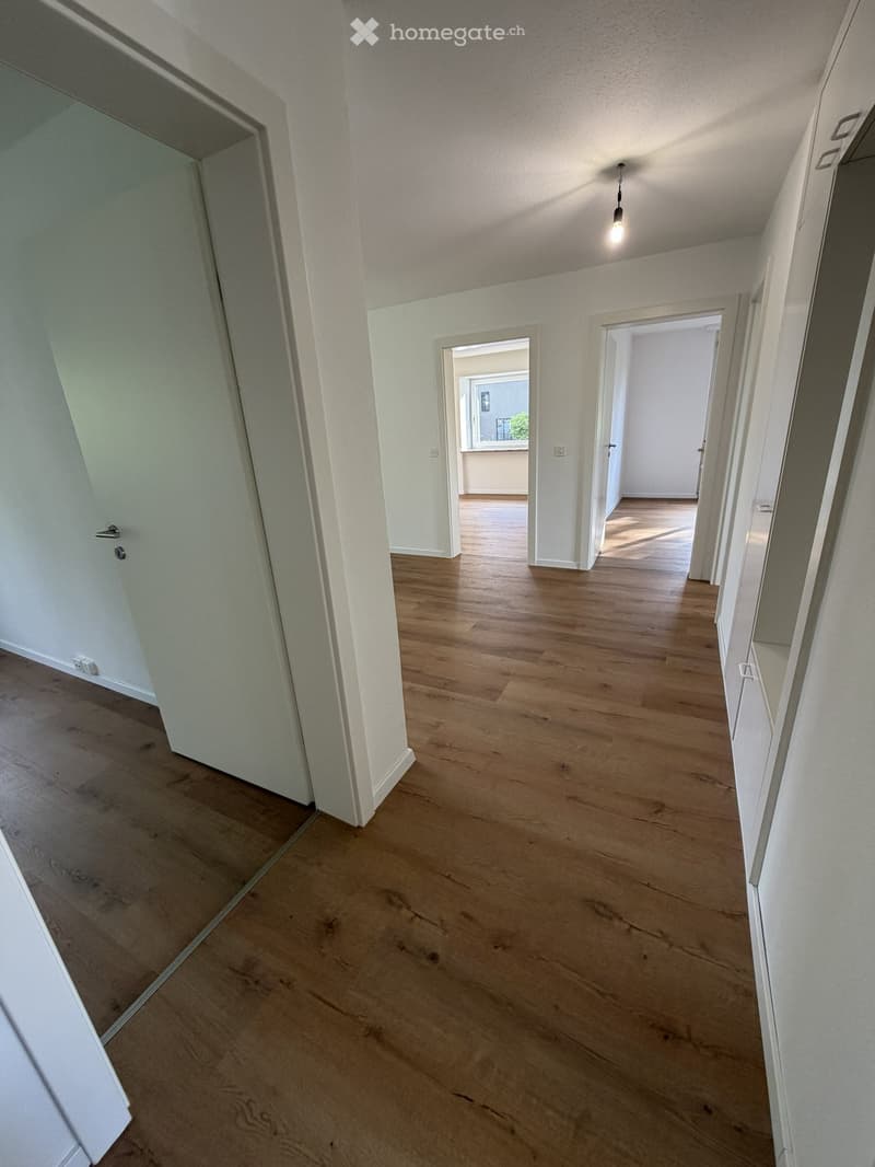 Empty hallway with wooden flooring, white walls, and several doors leading to other rooms.