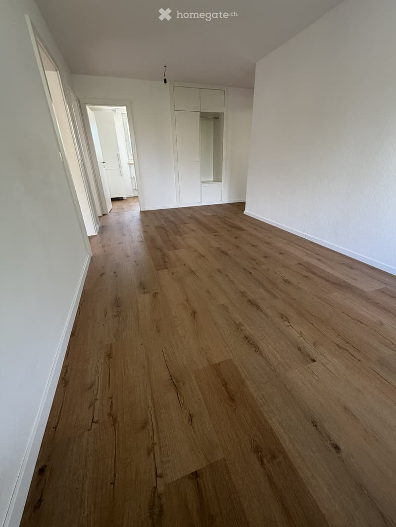 Empty hallway with wooden flooring and white walls, featuring a built-in wardrobe and open doorways leading to other rooms.