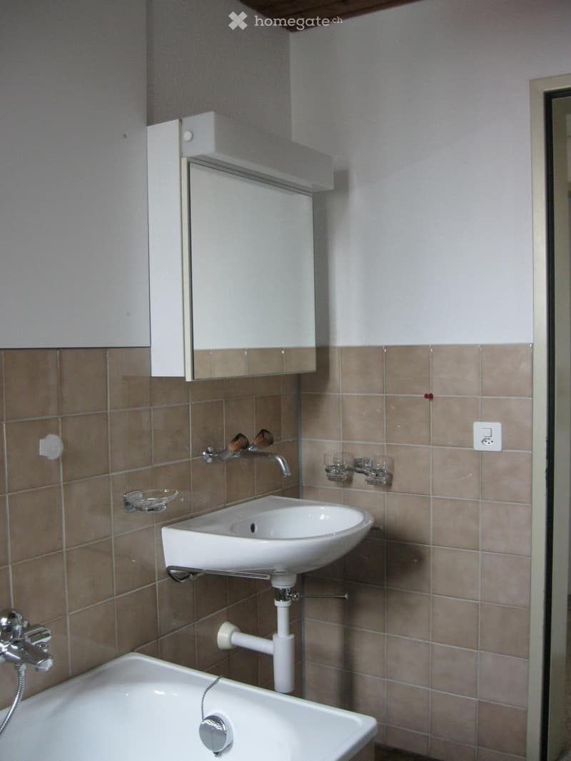 Bathroom with a white sink, bathtub, mirror, and cabinet. Beige tiled walls and modern fixtures.