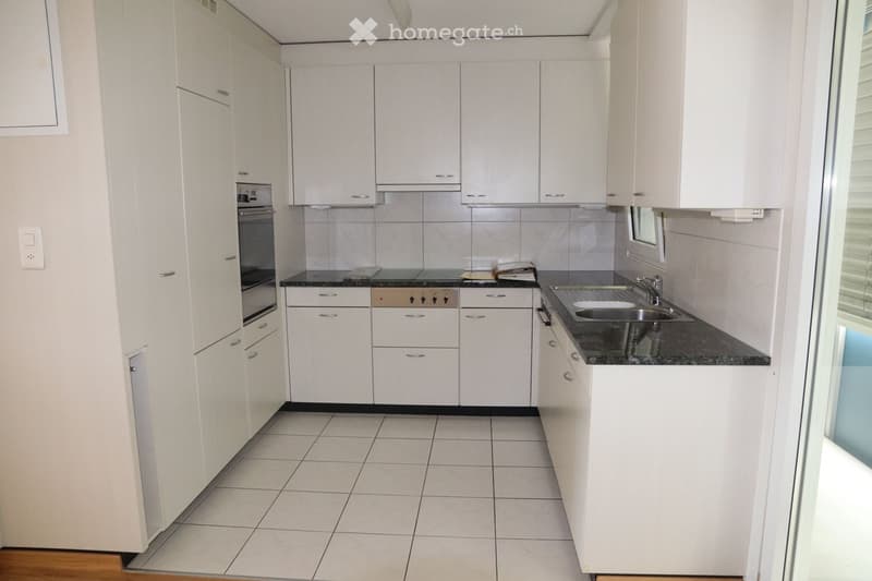 Modern kitchen with white cabinets, tiled floor, granite countertop, and stainless steel sink and oven.