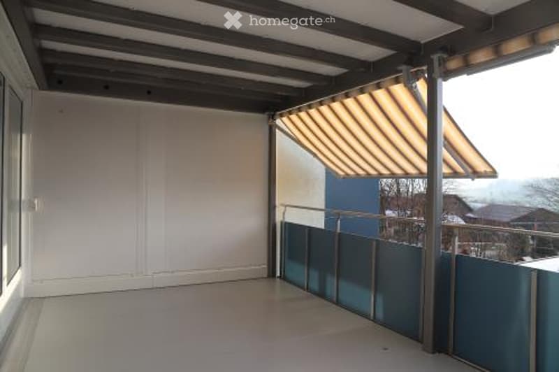 Empty balcony with retractable awning, blue fencing, white walls, and tiled floor