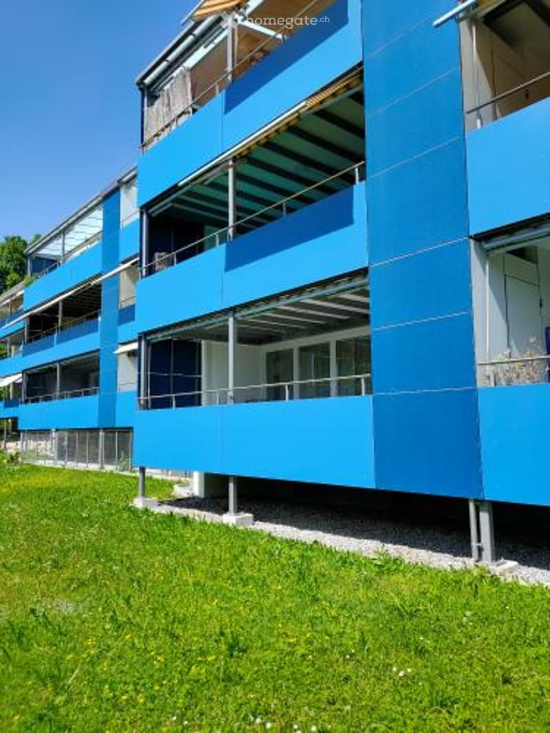 blue multi-story apartment building, balconies, metal railings, well-kept grassy area in front