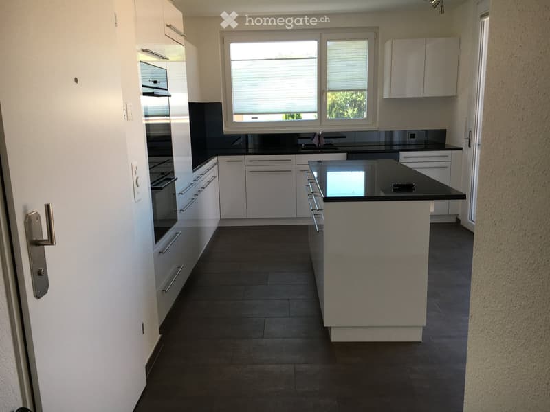 Modern kitchen with white cabinets, black countertops, and a central island. Features an oven, sink, and ample storage space.