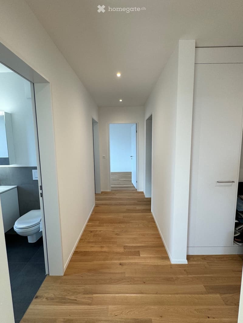 Empty hallway with wooden floor, white walls, and doors on both sides