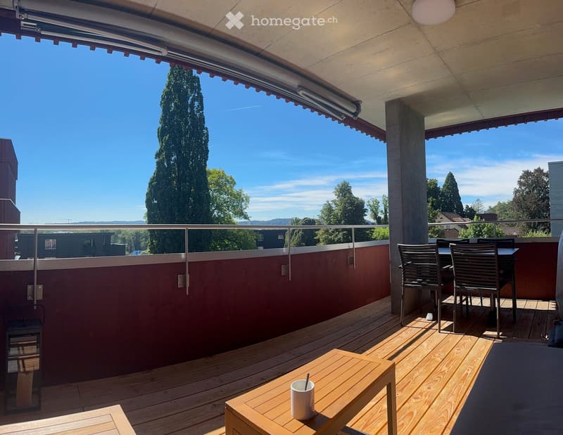 wooden deck, metal railing, table with a cup, chairs, table, red wall, trees, mountains